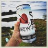 Man holding crowler of beer in front of him with water and sky in front of him