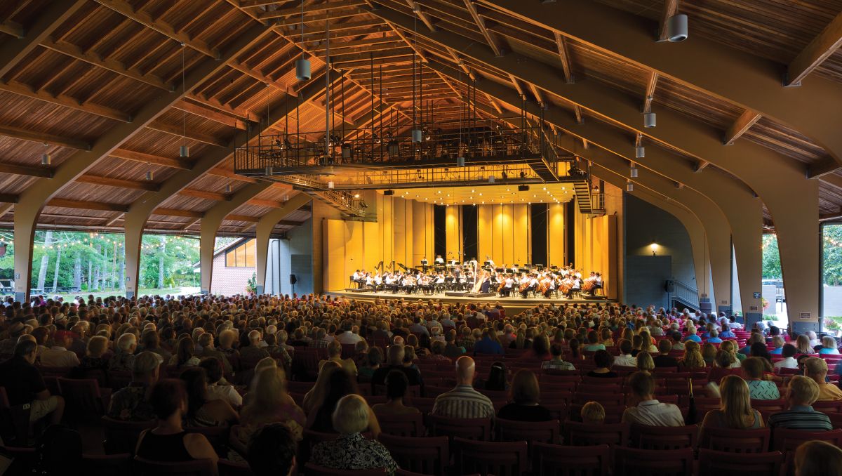 Concert being performed on stage of outdoor pavilion with full crowd in front of stage