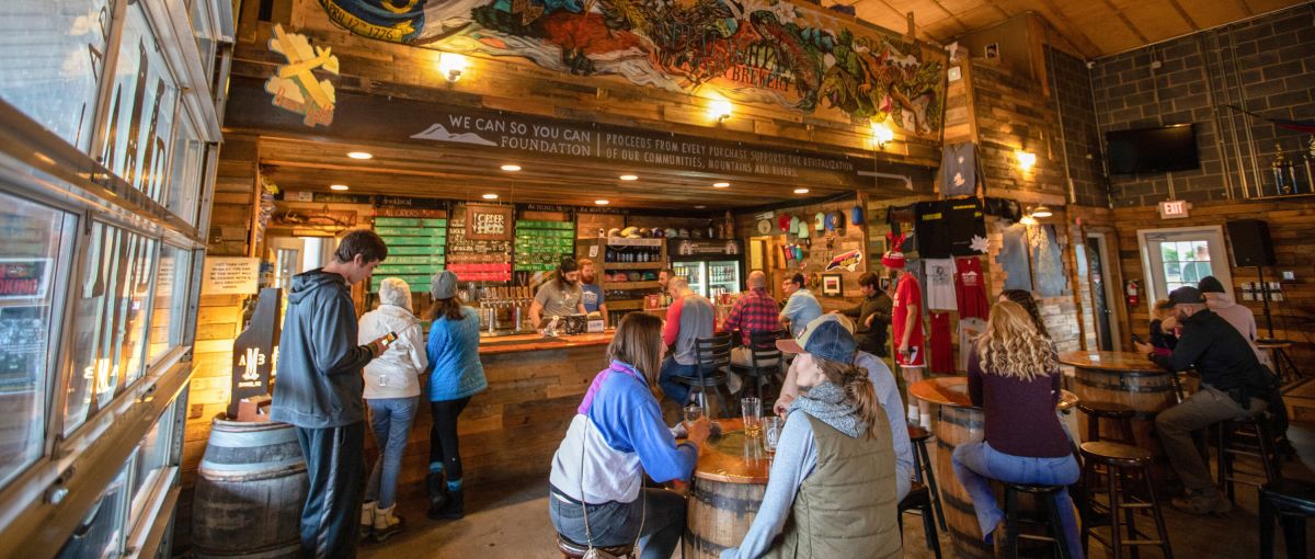 People enjoying beers inside at Appalachian Mountain Brewery, with hand-painted mural above bar