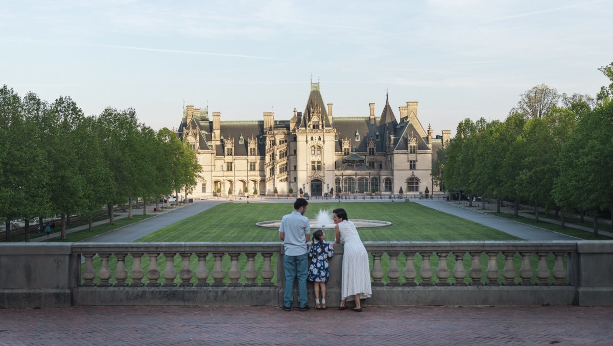 Family of 3 standing at stone wall overlooking Biltmore Estate and grounds