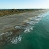 Aerial of beautiful, empty beach with waves rolling in and dunes in background