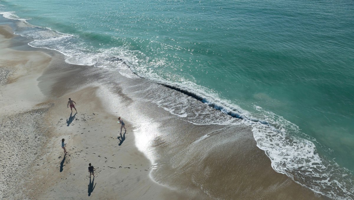 Aerial of family throwing frisbee on sand near clear, calm ocean