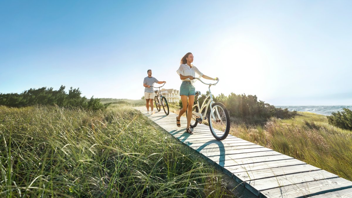 Couple walking bikes on wood walkway through marsh on Bald Head Island