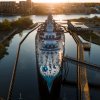 Aerial, straight-on shot of Battleship North Carolina in river with city in background.