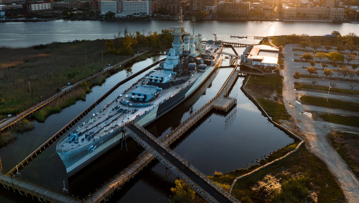 Aerial shot of Battleship North Carolina in river with city in background during daytime.