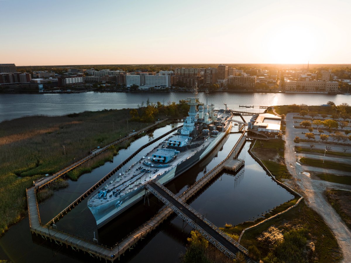 Aerial shot of Battleship North Carolina in river with city in background during daytime.