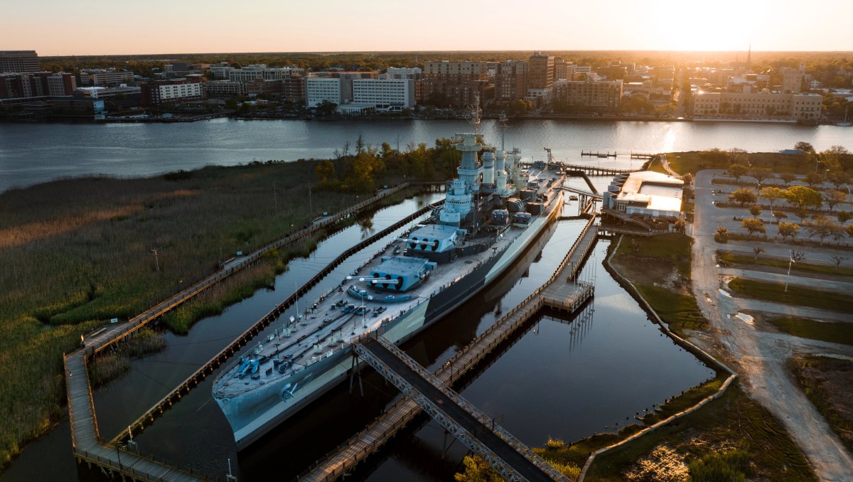 Aerial shot of Battleship North Carolina in river with city in background during daytime.