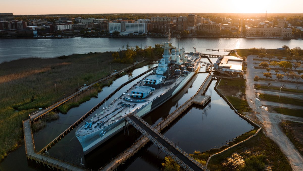 Aerial shot of Battleship North Carolina in river with city in background during daytime.