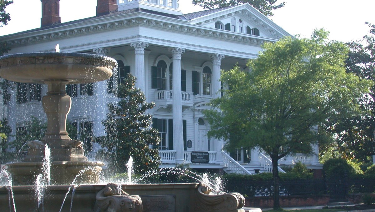 Large white mansion with fountain in forefront