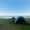 Blue tent set up on green grass with two camping chairs, sound and blue sky in background