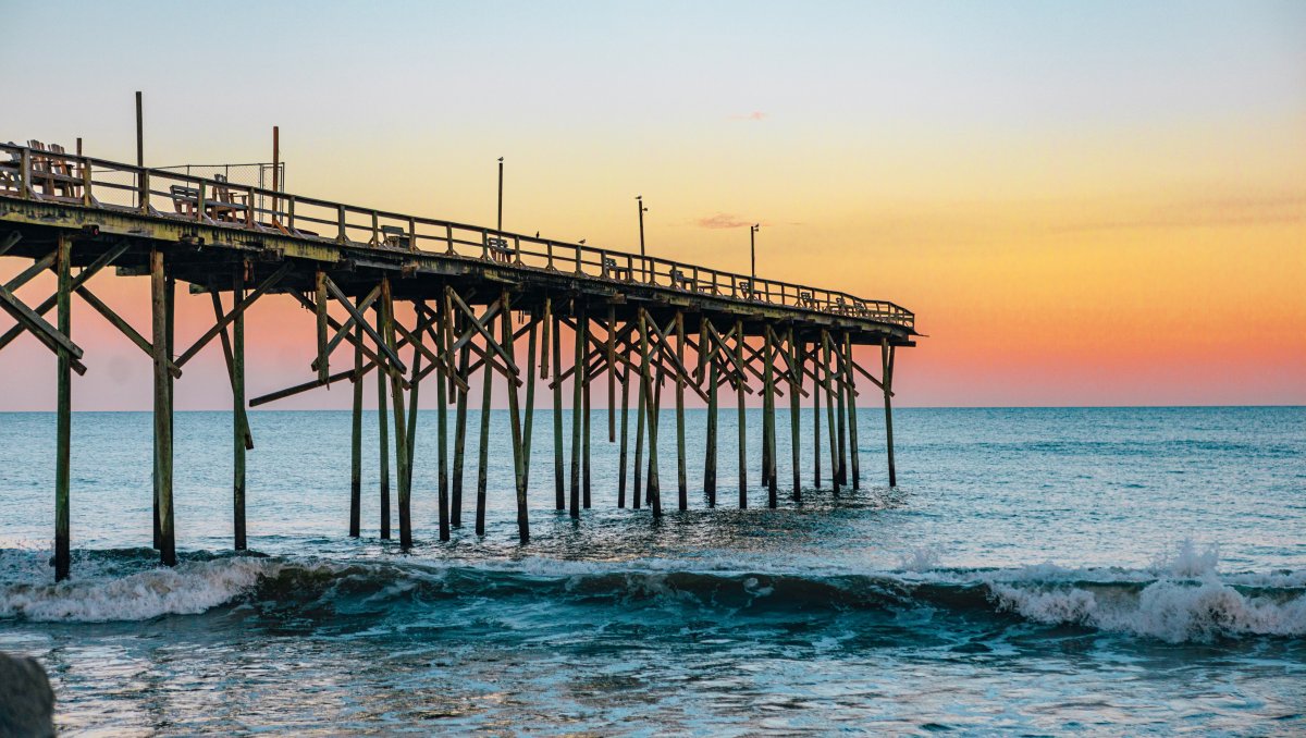 Wooden pier jutting out into ocean with beautiful orange and pink sky over ocean in distance