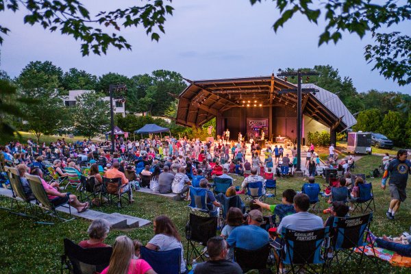 Crowd of people sitting on amphitheater lawn watching band perform at dusk