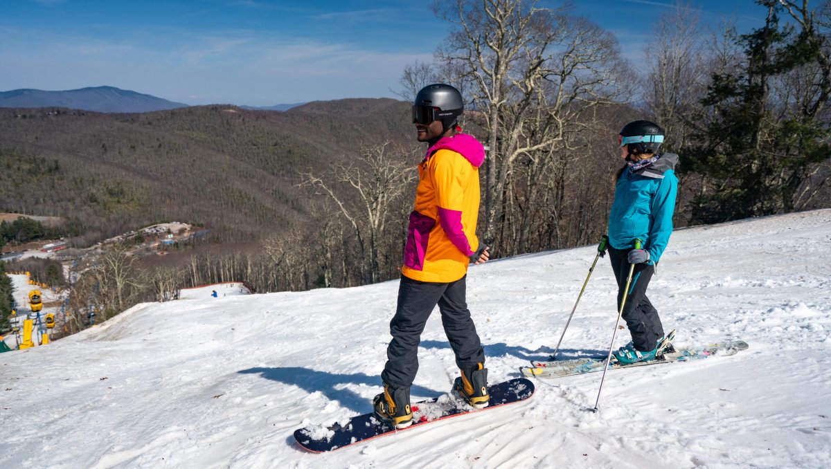 Couple standing at top of ski slope admiring the views of surrounding mountains, trees and ski slopes