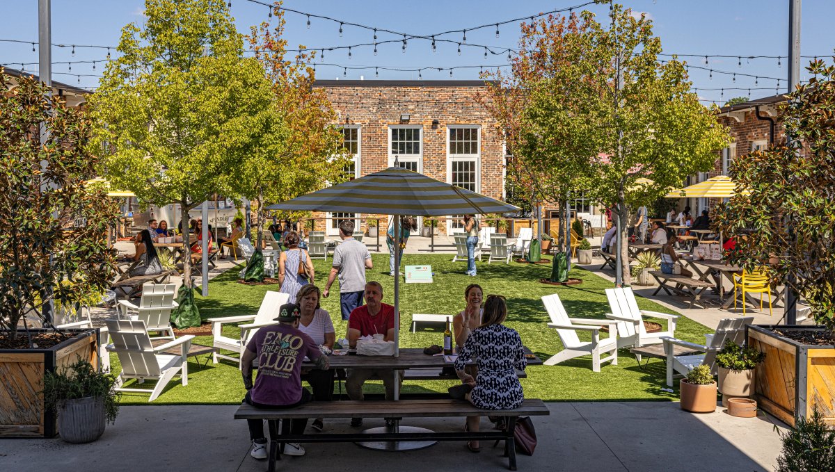 People sitting at tables and chairs outdoors in courtyard during daytime with trees and string lights