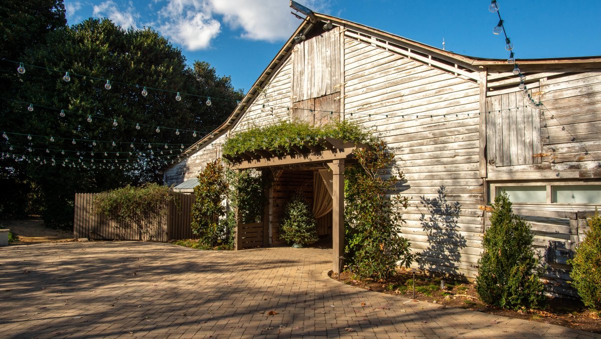 Exterior of rustic farm wedding venue with string lights over walkway