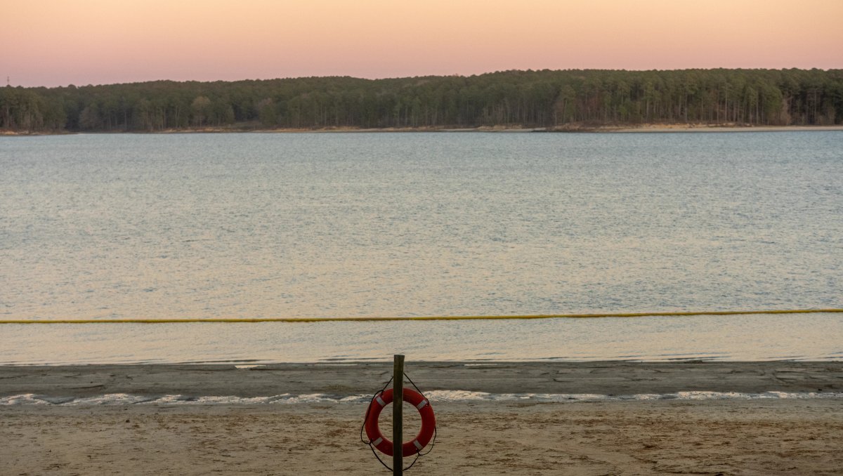 Pink and orange sky over beach and calm lake with shoreline in background