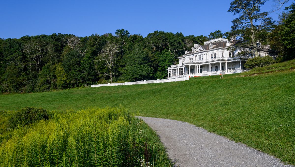 Large, white Cone Manor surrounded by lush, green grounds and trees in background on clear day