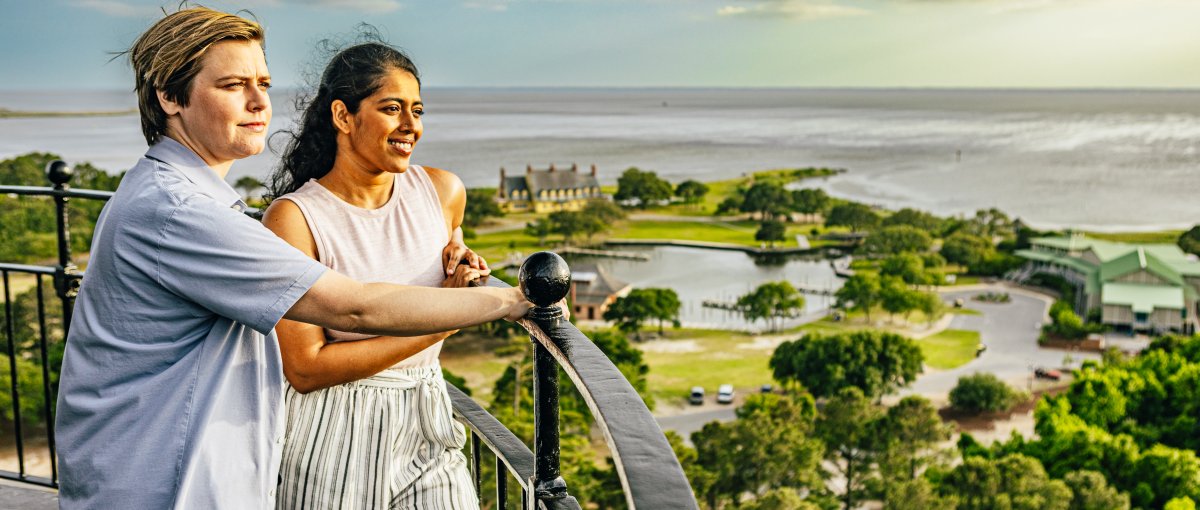 Couple standing at top of lighthouse with trees and ocean in background