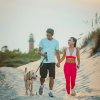 Couple walking dog on beach with lighthouse in background