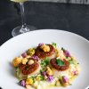 Plate of seared scallops and grits on table with glass of white wine