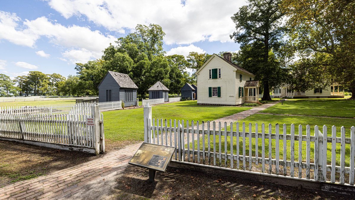 Historical marker in front of white fence and white historical buildings