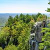 Woman sitting on edge of cliff at Crowders Mountain with trees all around on sunny day