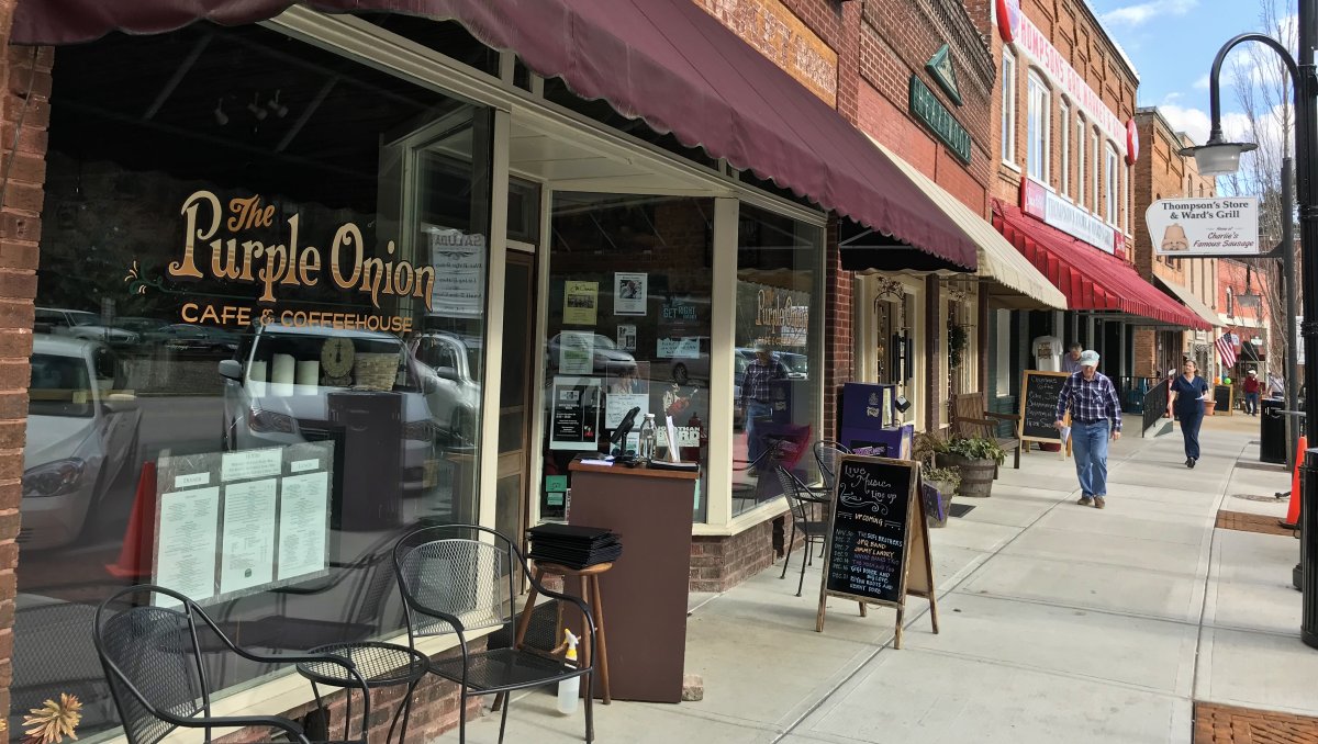 Exterior of cafe with seating outside, with people walking down sidewalk