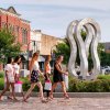 Group of five women walking through downtown area with art and shops in background