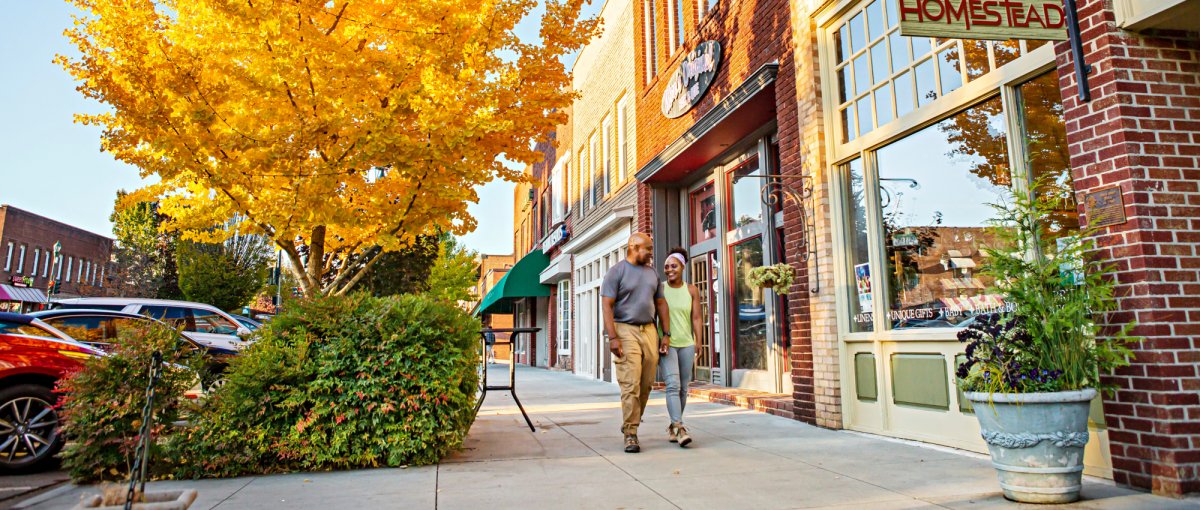 Couple holding hands walking down sidewalk on Main Street in downtown Hendersonville in fall