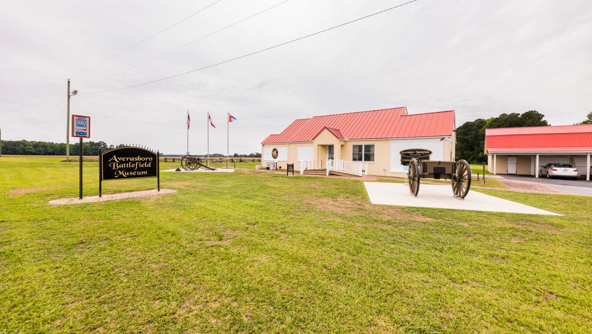 Exterior of Averasboro Battlefield Museum with signage, cannons and flags in front of museum