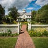 Straight-on shot of exterior of Cupola House, with white picket fence and gardens in front of house during cloudy daytime