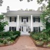 Front exterior of a beautiful white inn, with gardens and brick sidewalk in front during daytime