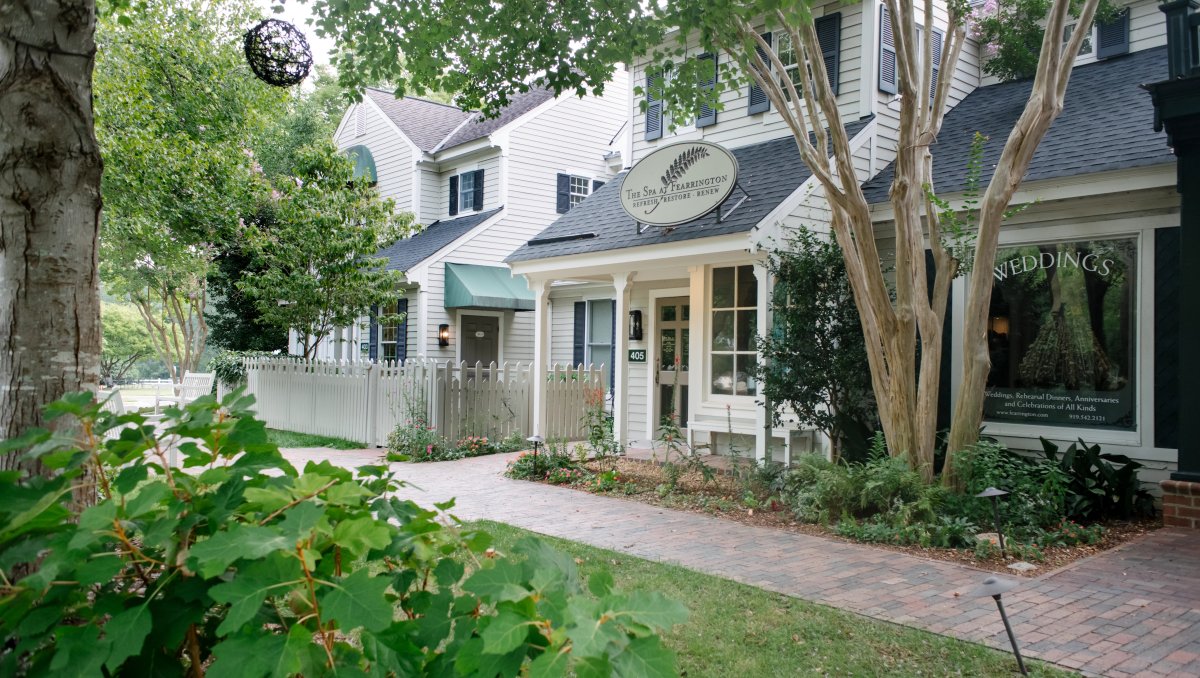 Exterior of spa with brick sidewalk in front of white buildings, with trees surrounding buildings