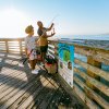 Grandfather and granddaughter admiring freshly caught fish on pole while standing on fishing pier