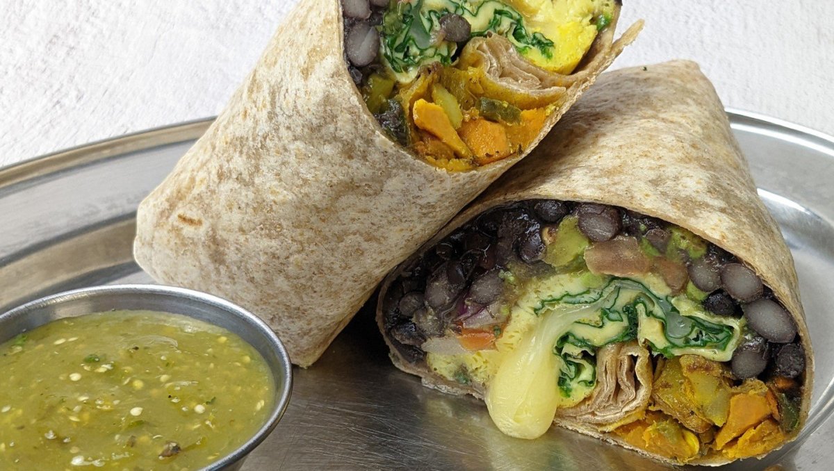 Closeup of vegan burrito on a plate next to salsa verde