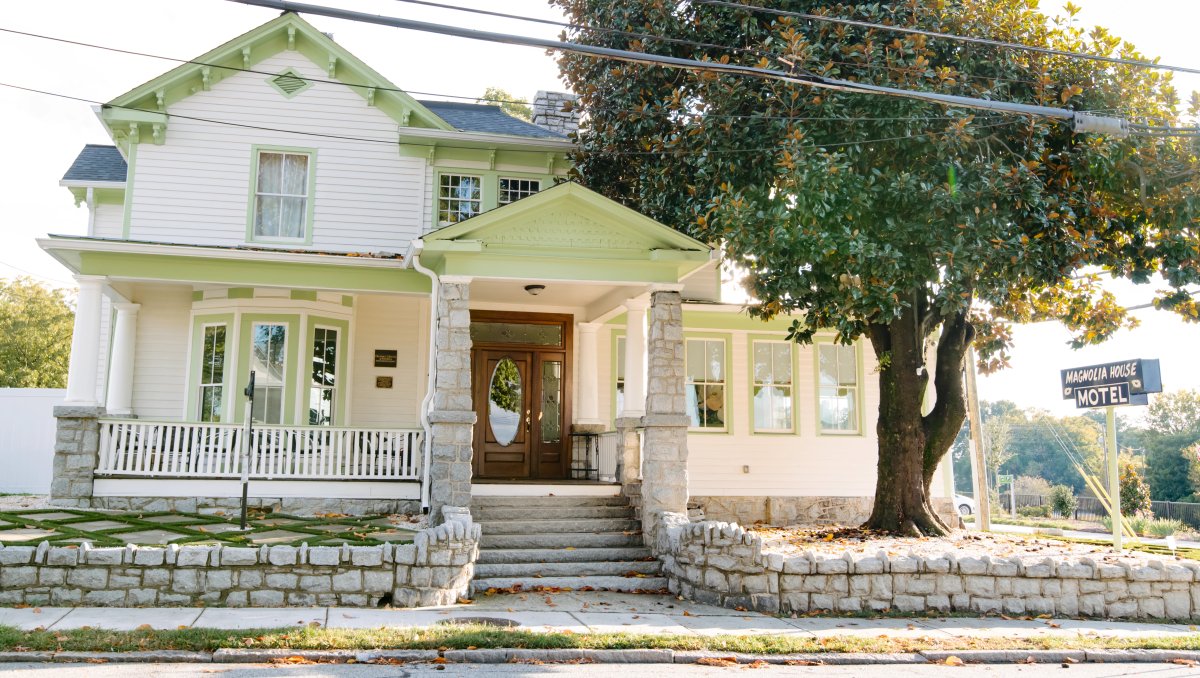 Exterior of white and green historic Magnolia House with tree in front year