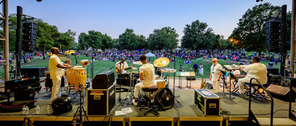 Band playing on stage looking out onto tons of people sitting on lawn enjoying show