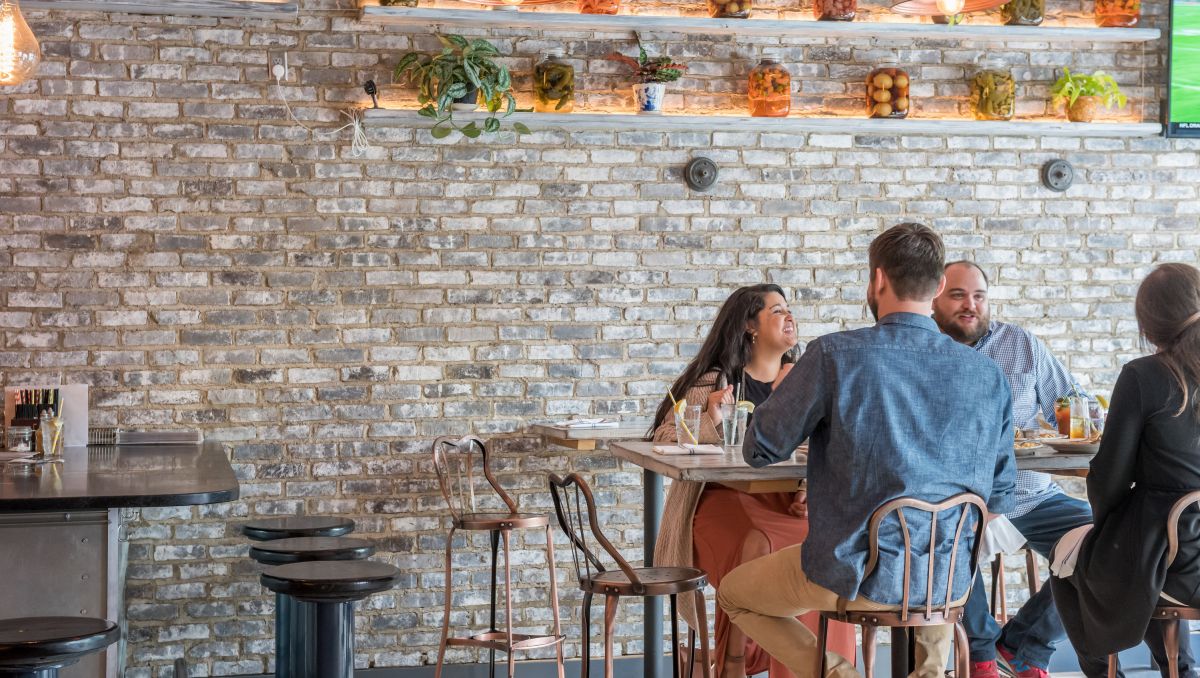 Friends enjoying a meal at Haberdish with gray brick wall behind them