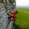 Man in red shirt rock climbing in Hanging Rock State Park with valley and trees below on bright day