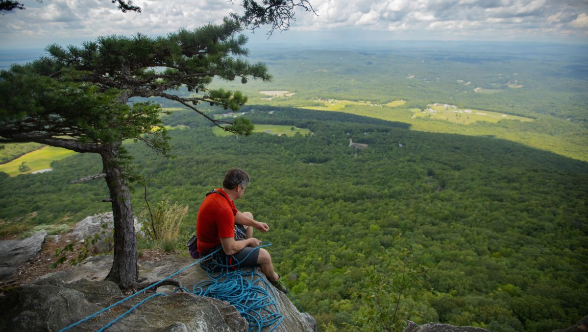 Man sitting on edge of cliff looking down to the valley during daytime