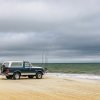 Ford Bronco along beach with cloudy, stormy skies over ocean.