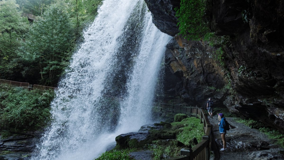 Woman standing in walking path behind and under large waterfall