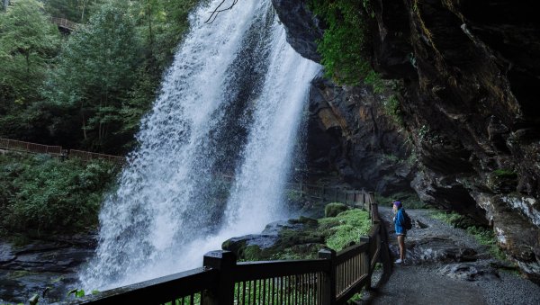 Woman standing in walking path behind and under large waterfall