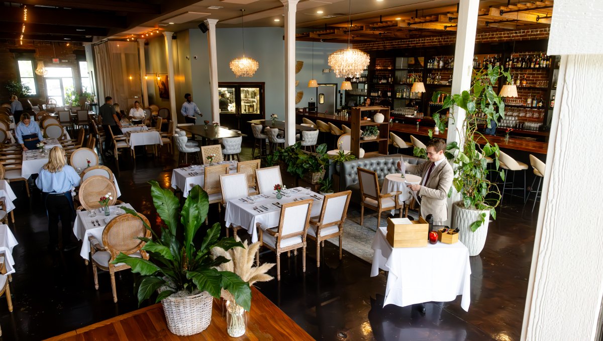 Interior of high-end restaurant filled with tables and diners with bar in background