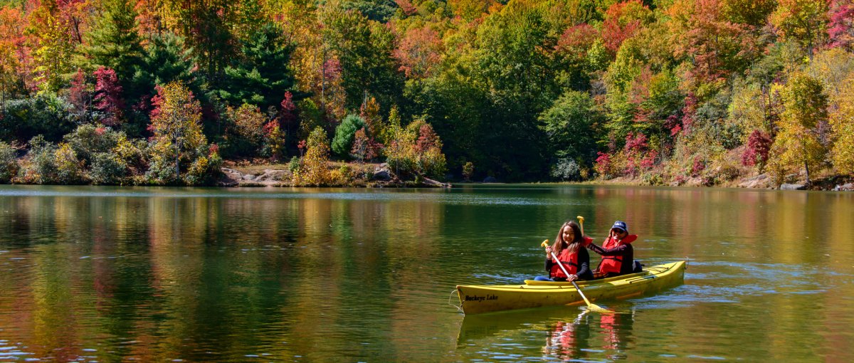 Two friends kayaking in calm lake surrounded by bright fall foliage