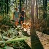 Wide shot of LGBTQ+ couple walking dog on wooden trail in Howell Woods.