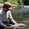 Man standing in river looking down at fish he's holding