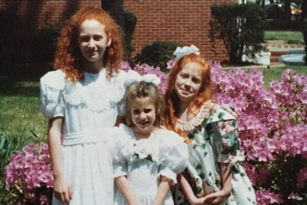 Three sisters in dresses standing in front of pink blooming flowers