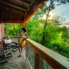 Man and woman drinking wine on the porch of a treehouse with green trees in background