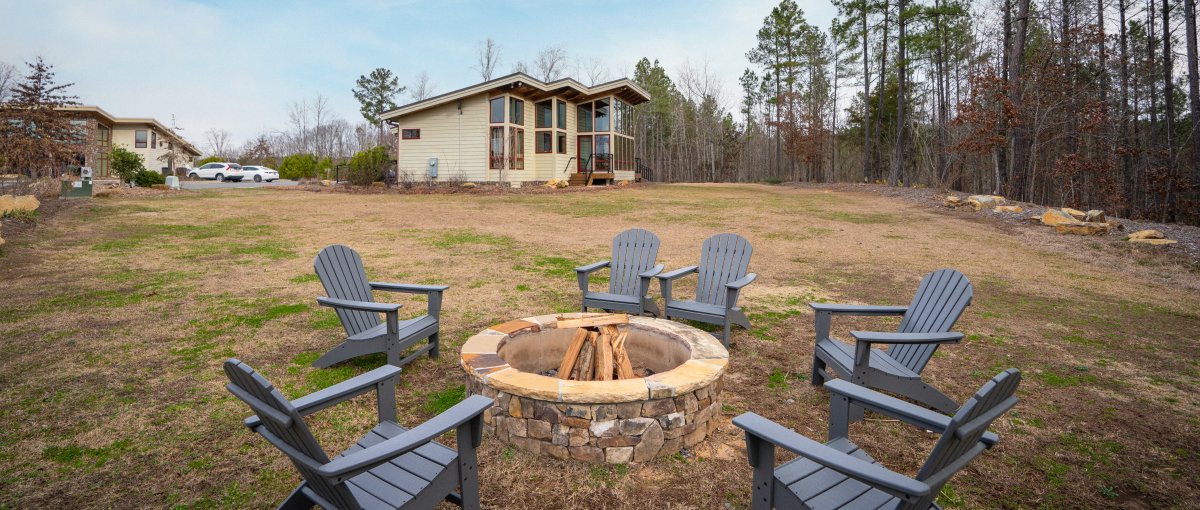 Adirondack chairs around fire pit on farm's grounds with cabin in background